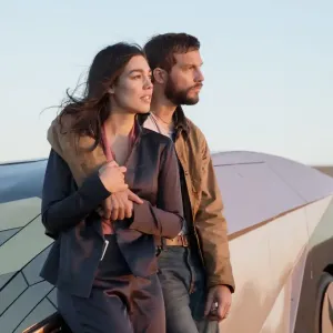 A man and a woman lean on a car outside in Upgrade.