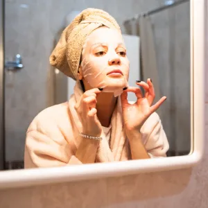 Woman applying a sheet mask in the bathroom mirror