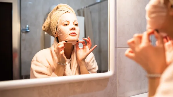 Woman applying a sheet mask in the bathroom mirror