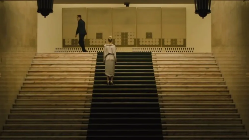 A woman looks at a man on stairs in Watcher.
