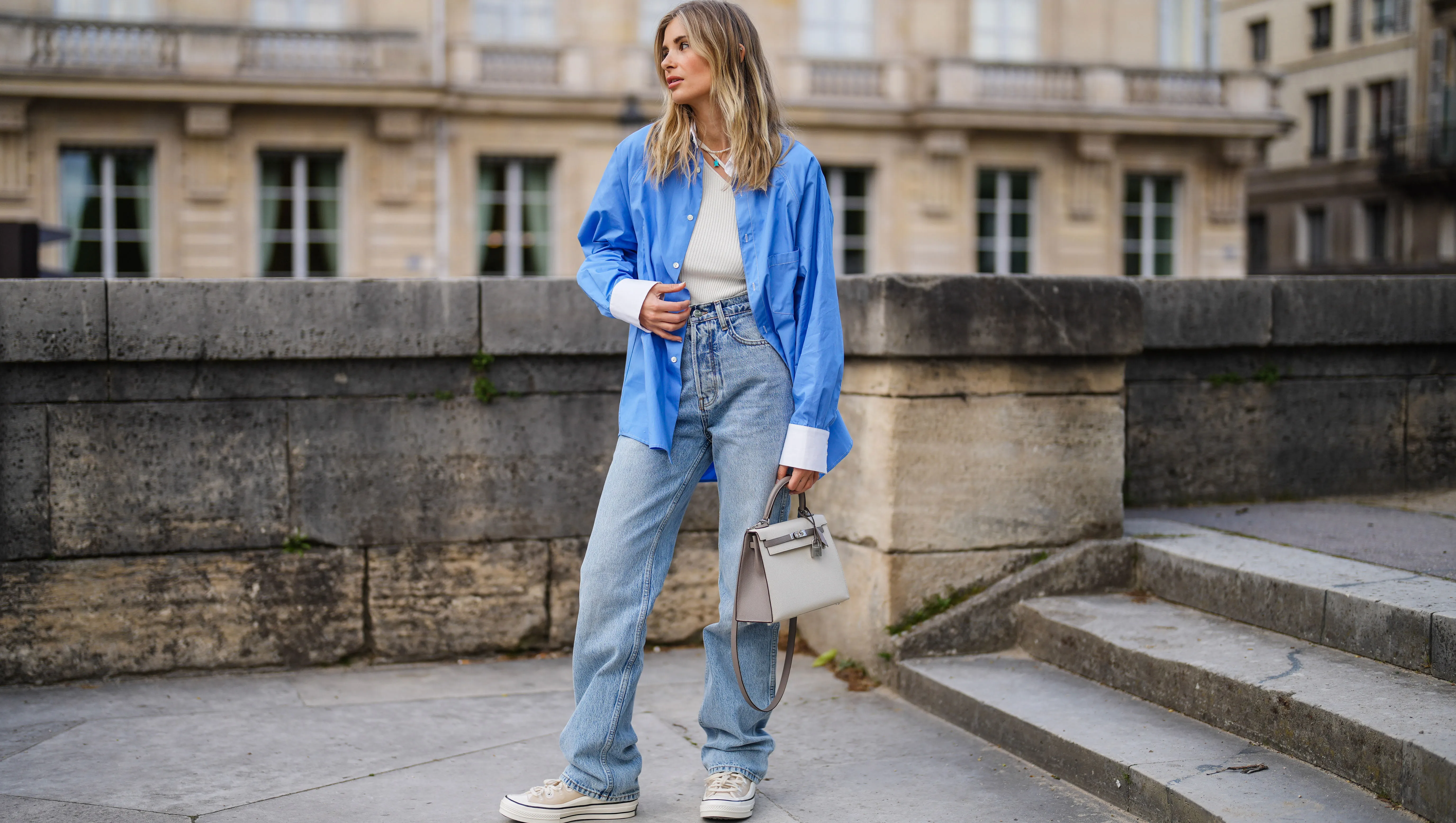 PARIS, FRANCE - MAY 10: Xenia Adonts wears a blue oversized long shirt with white collar and white cuffs from Attire The Studio, a white ribbed asymmetric top from Attire The Studio, blue denim jeans wide-leg pants from Anine Bing, a beige Kelly Hermes bag, sneakers from Converse x Kim Jones, on May 10, 2021 in Paris, France. (Photo by Edward Berthelot/Getty Images)