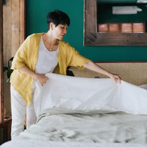 Senior Asian woman doing her morning routine, making up her bed at home. Let's get the day started - stock photo
