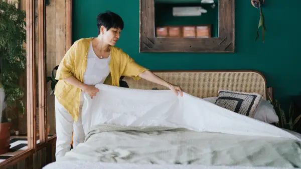 Senior Asian woman doing her morning routine, making up her bed at home. Let's get the day started - stock photo