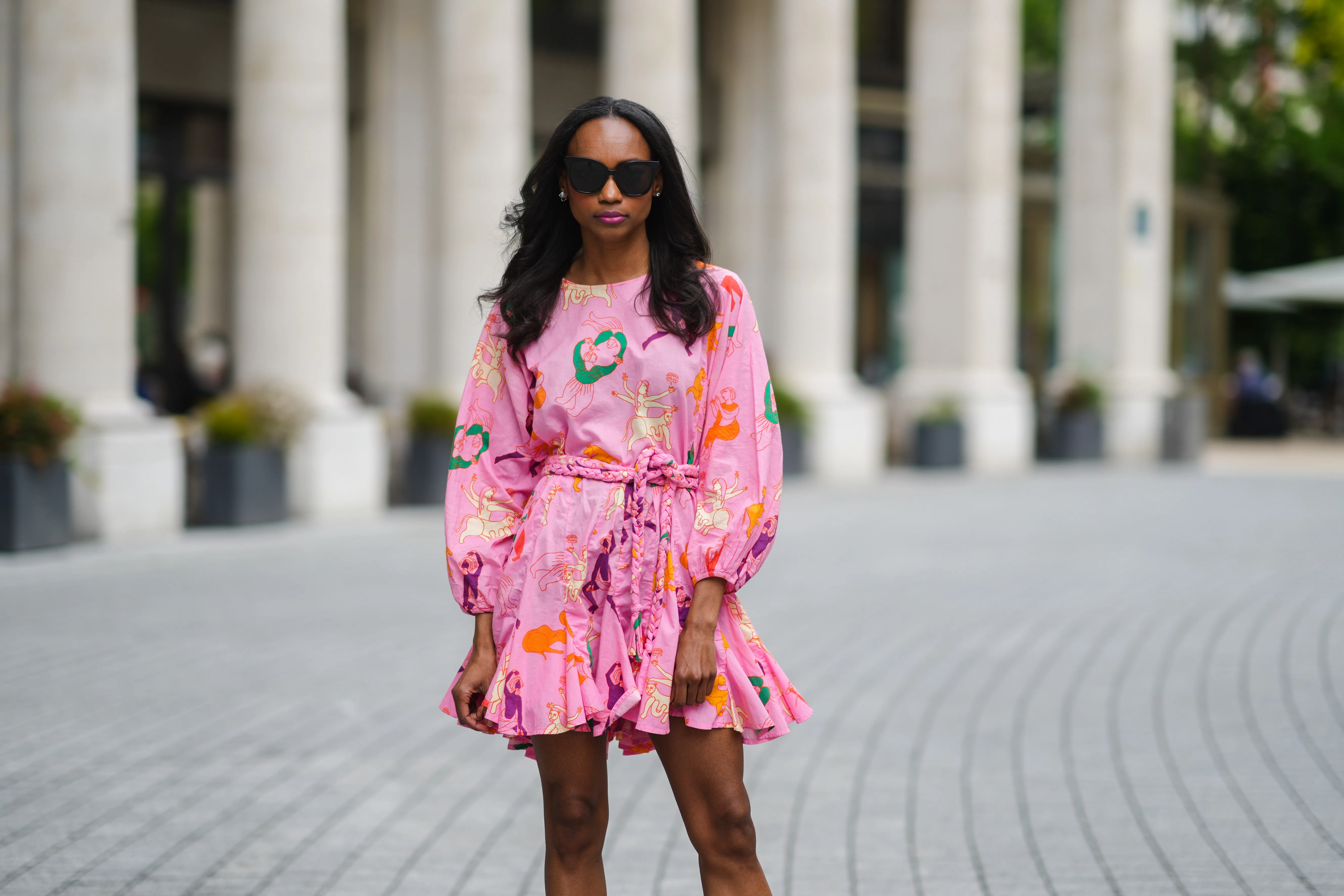 Emilie Joseph @in_fashionwetrust wears sunglasses, silver earrings, a Rhode printed summer vacay Ella dress in vibrant pink with long dolman sleeves with elastic cuffs and a full a flirty hem and a waist-cinching braided belt, on May 27, 2021 in Paris, France.