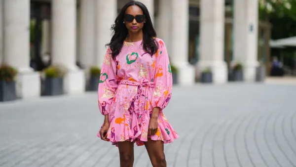 Emilie Joseph @in_fashionwetrust wears sunglasses, silver earrings, a Rhode printed summer vacay Ella dress in vibrant pink with long dolman sleeves with elastic cuffs and a full a flirty hem and a waist-cinching braided belt, on May 27, 2021 in Paris, France.