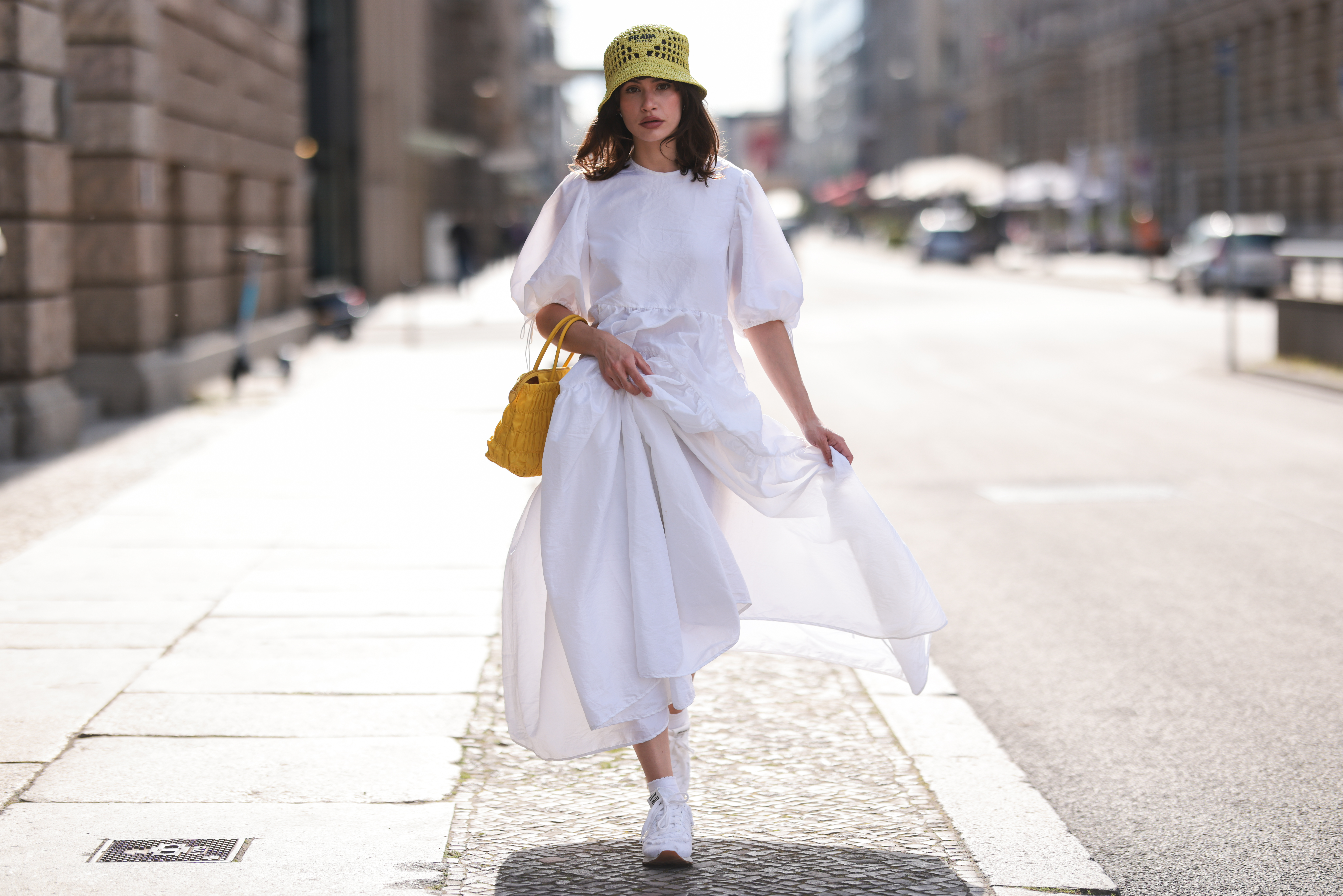 Lena Naumann wearing New Balance x Miu Miu white sneaker, Cecilie Bahnsen white maxi dress, Prada kiwi green bucket hat, Prada yellow bag on May 31, 2022 in Berlin, Germany.