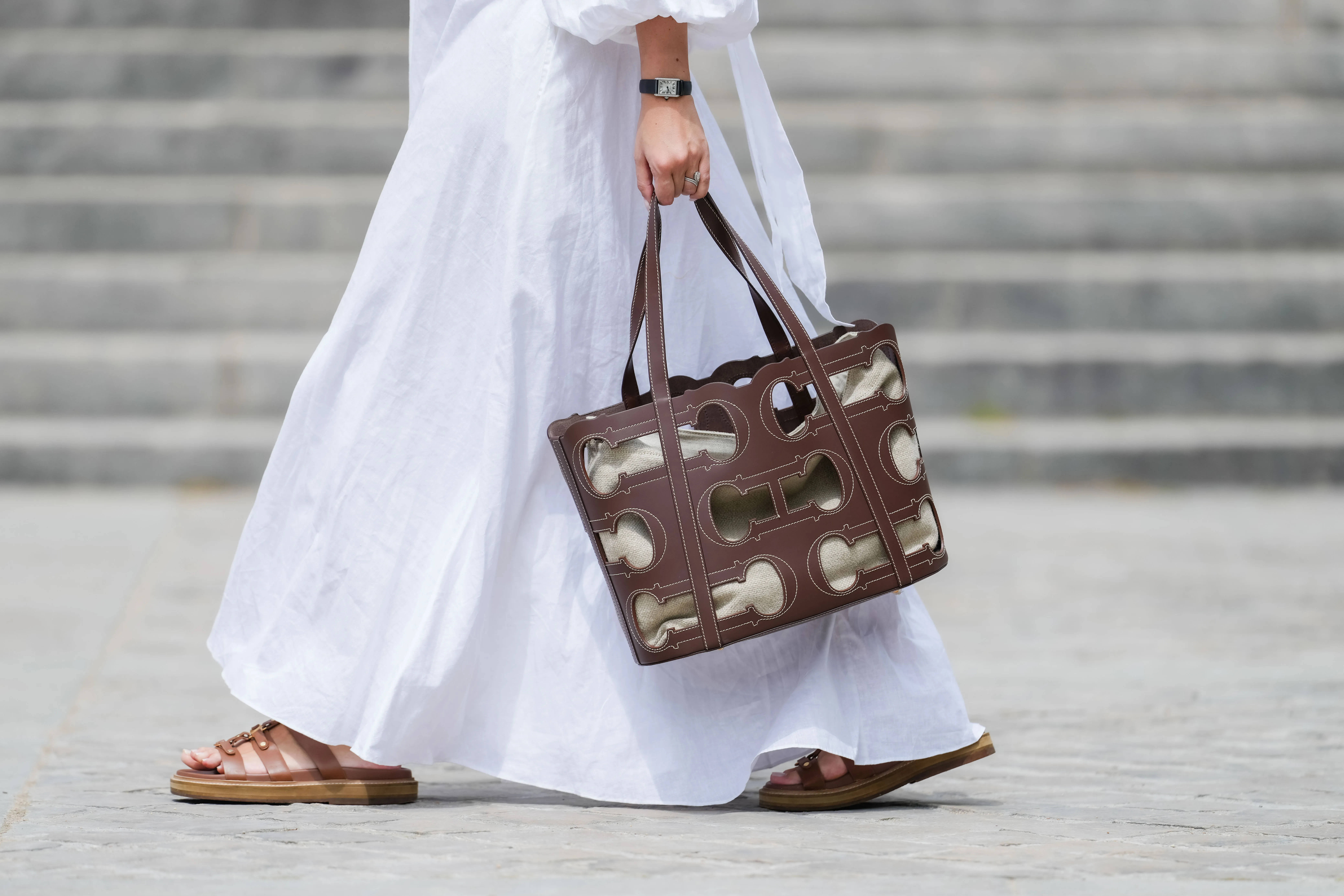 Gabriella Berdugo wears a Cartier watch, a white linen gathered dress from kalita, a brown summer bag from Carolina Herrera in brown leather, brown leather sandals from Celine, during a street style fashion photo session, on May 12, 2024 in Paris, France.