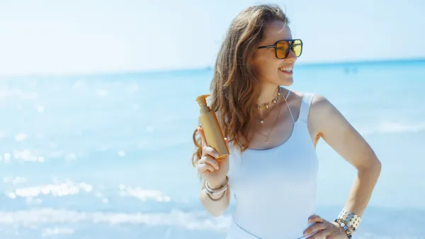 Smiling stylish female on seashore with spf - stock photo