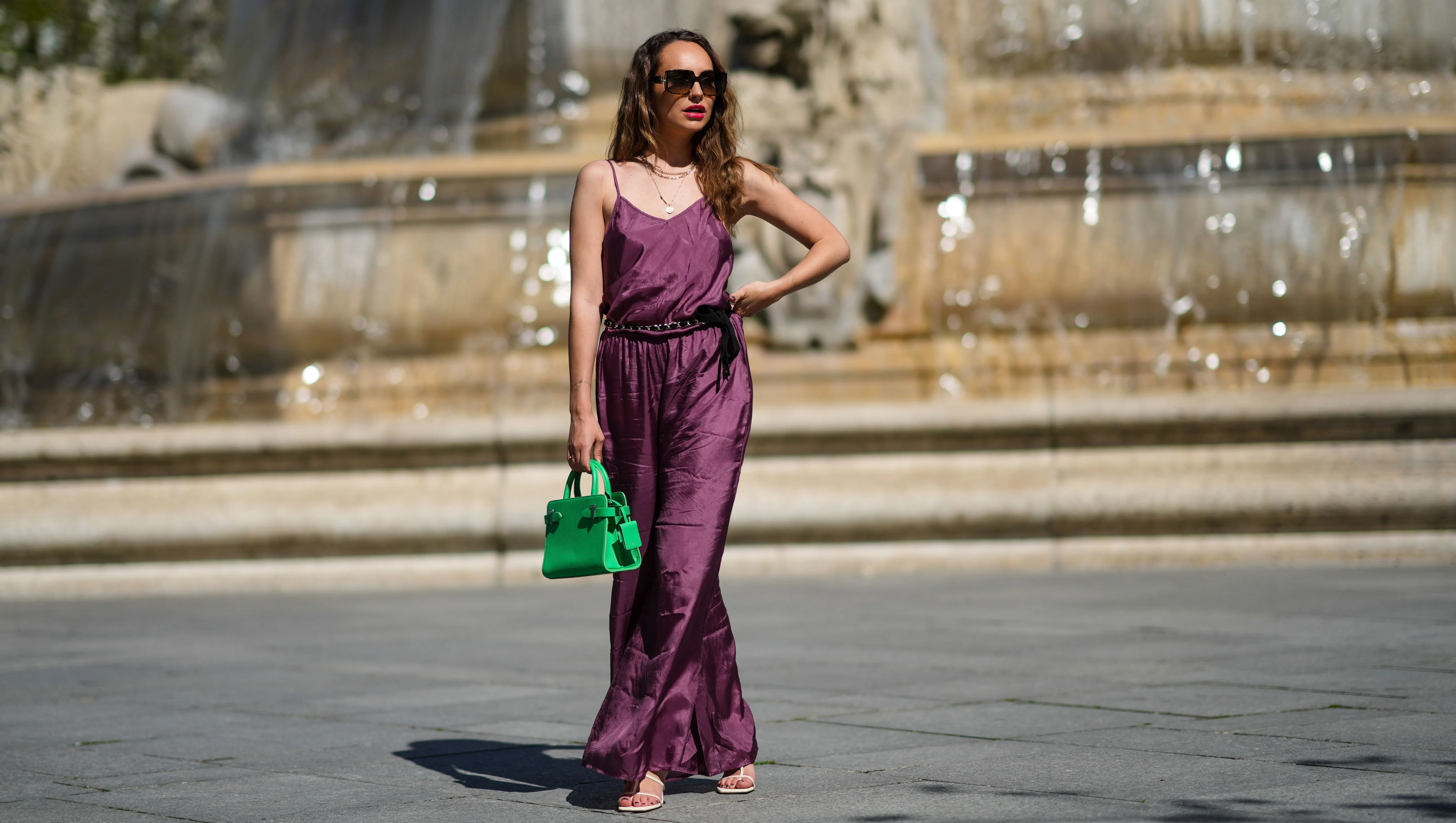 PARIS, FRANCE - MARCH 30: Ophélie Duvillard wears sunglasses, a necklace, a purple satin silky shiny jumpsuit from Mes Demoiselles with a tank top upper part and a lower part made of flared flowing pants, a Chanel belt, a neon green leather bag from Le Tanneur, shoes from Zara, on March 30, 2021 in Paris, France. (Photo by Edward Berthelot/Getty Images)