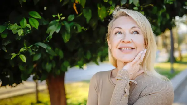 Natural beauty care: Beautiful blonde woman poses near a green tree in summer, emphasizing her natural approach to body and skincare - stock photo