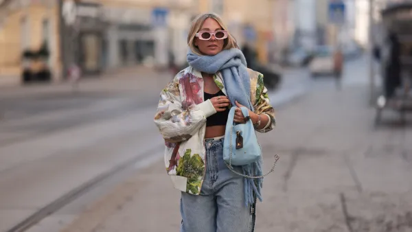 VIENNA, AUSTRIA - FEBRUARY 19: Karin Teigl seen wearing Loewe light pink sunglasses, black cotton crop top, Stine Goya cream white colorful flower pattern quilted bomber jacket, Mango light blue oversized wool scarf, Miu Miu white cotton logo print underwear, H2O Fagerholt light blue oversized straight leg jeans with cut-outs, Louis Vuitton bag light blue leather crossbody bag with brown monogram canvas bag accessory and Valentino animal pattern Rockstud heels, on February 19, 2025 in Vienna, Austria. (Photo by Jeremy Moeller/Getty Images)