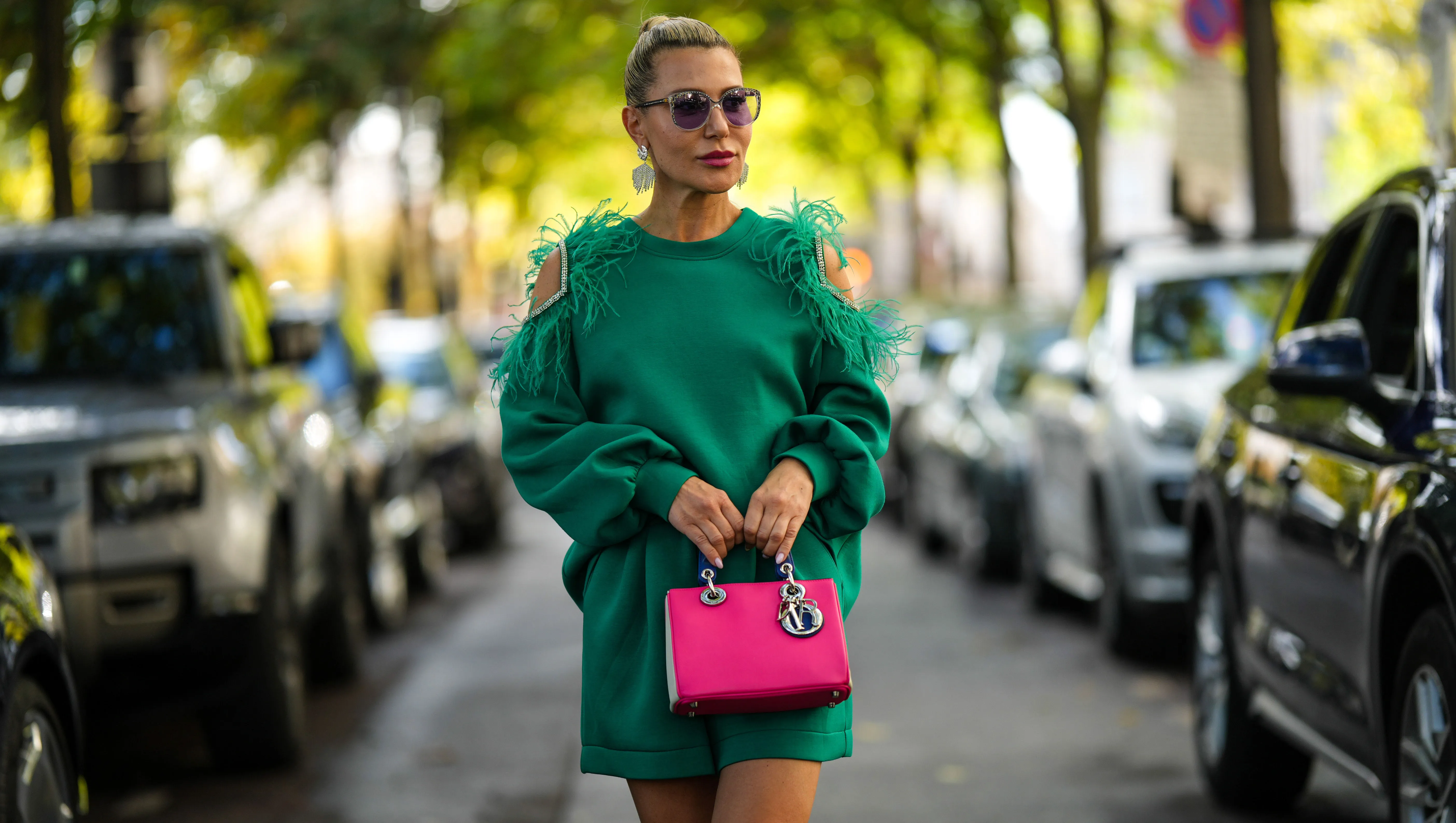 PARIS, FRANCE - OCTOBER 01: Olga Ferrara wears black circle sunglasses, silver rhinestones fringed earrings, a green cut-out shoulder / embroidered feather / embroidered rhinestones / belted short jumpsuit, a neon pink / beige / navy blue shiny leather handbag from Dior, outside Elie Saab, during Paris Fashion Week - Womenswear Spring/Summer 2023, on October 01, 2022 in Paris, France. (Photo by Edward Berthelot/Getty Images)