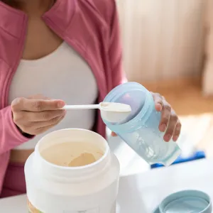 A healthy and fit Asian woman in sportswear making her protein shake after a workout at home. - stock photo