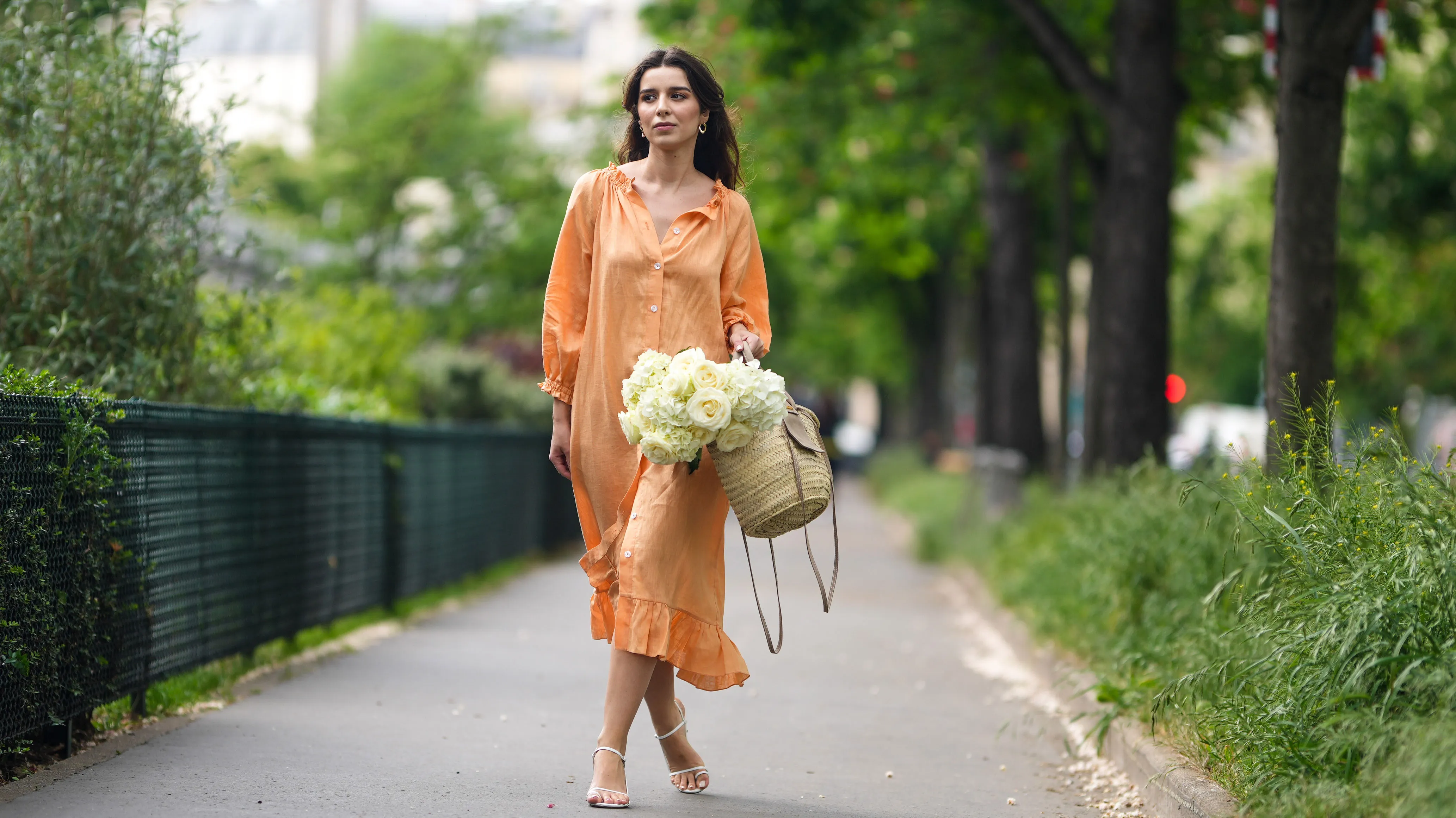 PARIS, FRANCE - MAY 10: Ketevan Giorgadze @katie.one wears gold earrings, a long buttoned coral loungewear linen The Sleeper dress with puffy sleeves, gold rings, a wicker with brown shiny leather detail Le Panier Soleil Jacquemus tote-bag, white strappy low heeled Raye sandals, on May 10, 2021 in Paris, France. (Photo by Edward Berthelot/Getty Images)