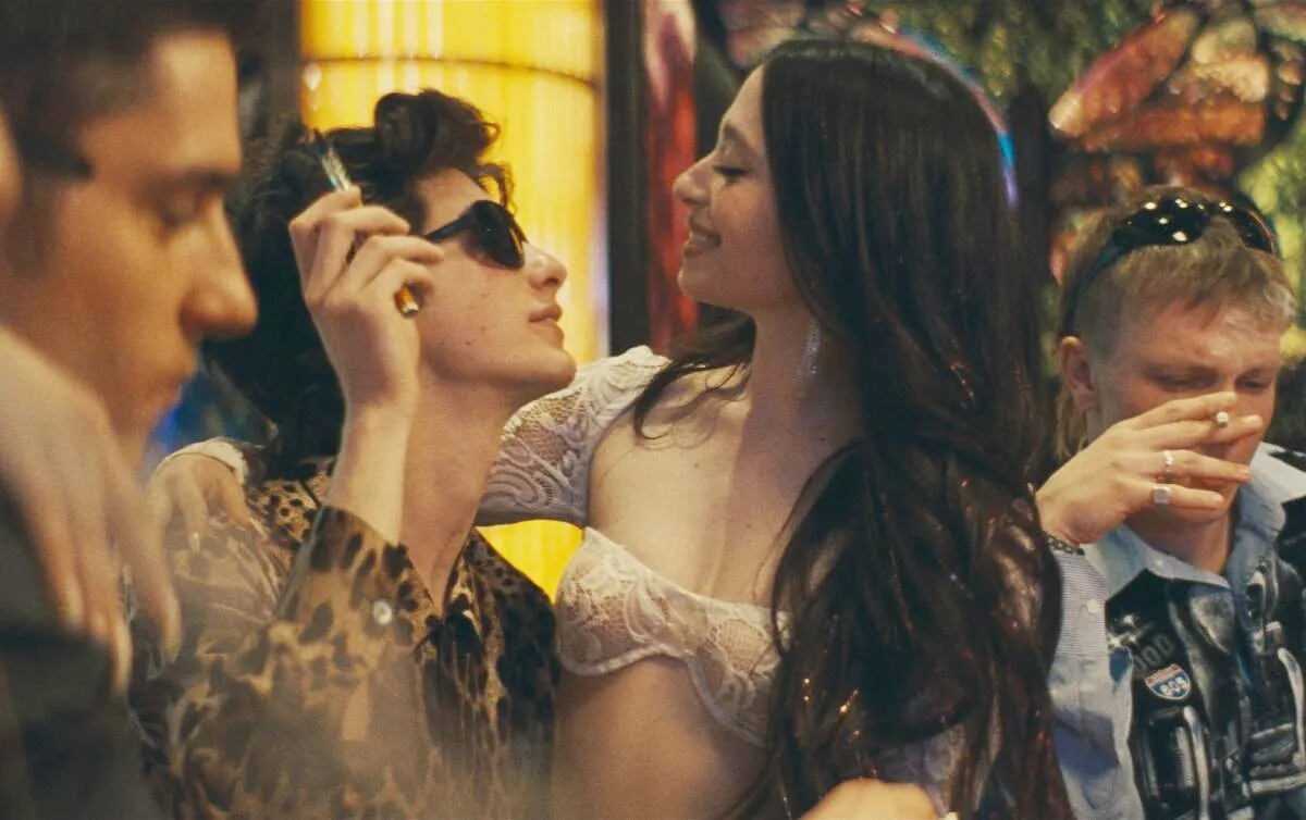 A woman sits and looks at a man smoking in 'Anora.'