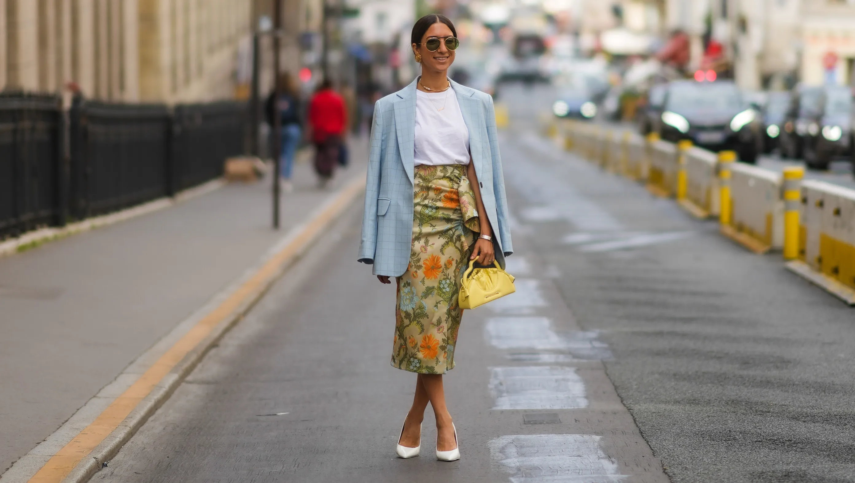 PARIS, FRANCE - JULY 07: A guest wears black sunglasses, a white t-shirt, a pale blue checkered pattern long blazer jacket, gold necklaces, gold earrings, a silver bracelet, a pale yellow with green and orange flower print patter wrap ruffled silk midi skirt, a yellow shiny leather handbag, white leather pointed pumps heels shoes, outside Zuhair Murad, during Paris Fashion Week - Haute Couture Fall/Winter 2021/2022, on July 07, 2021 in Paris, France. (Photo by Edward Berthelot/Getty Images)