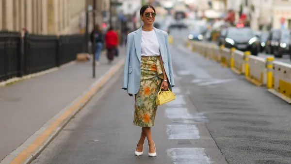 PARIS, FRANCE - JULY 07: A guest wears black sunglasses, a white t-shirt, a pale blue checkered pattern long blazer jacket, gold necklaces, gold earrings, a silver bracelet, a pale yellow with green and orange flower print patter wrap ruffled silk midi skirt, a yellow shiny leather handbag, white leather pointed pumps heels shoes, outside Zuhair Murad, during Paris Fashion Week - Haute Couture Fall/Winter 2021/2022, on July 07, 2021 in Paris, France. (Photo by Edward Berthelot/Getty Images)
