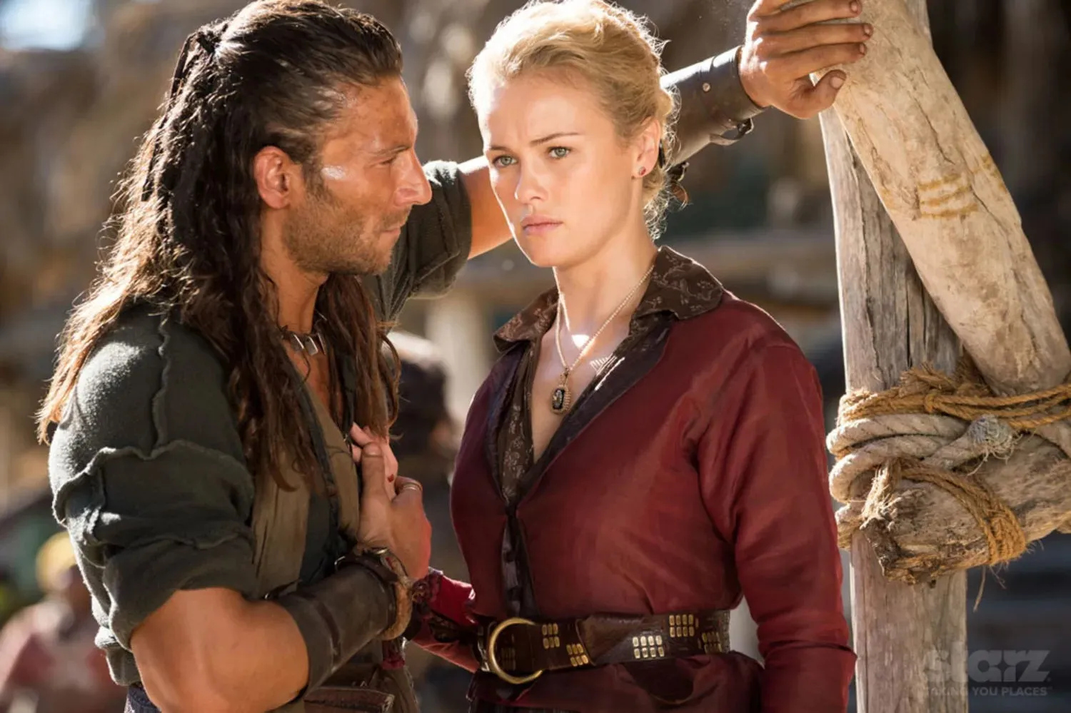 A pirate stands in front of a woman in Black Sails.