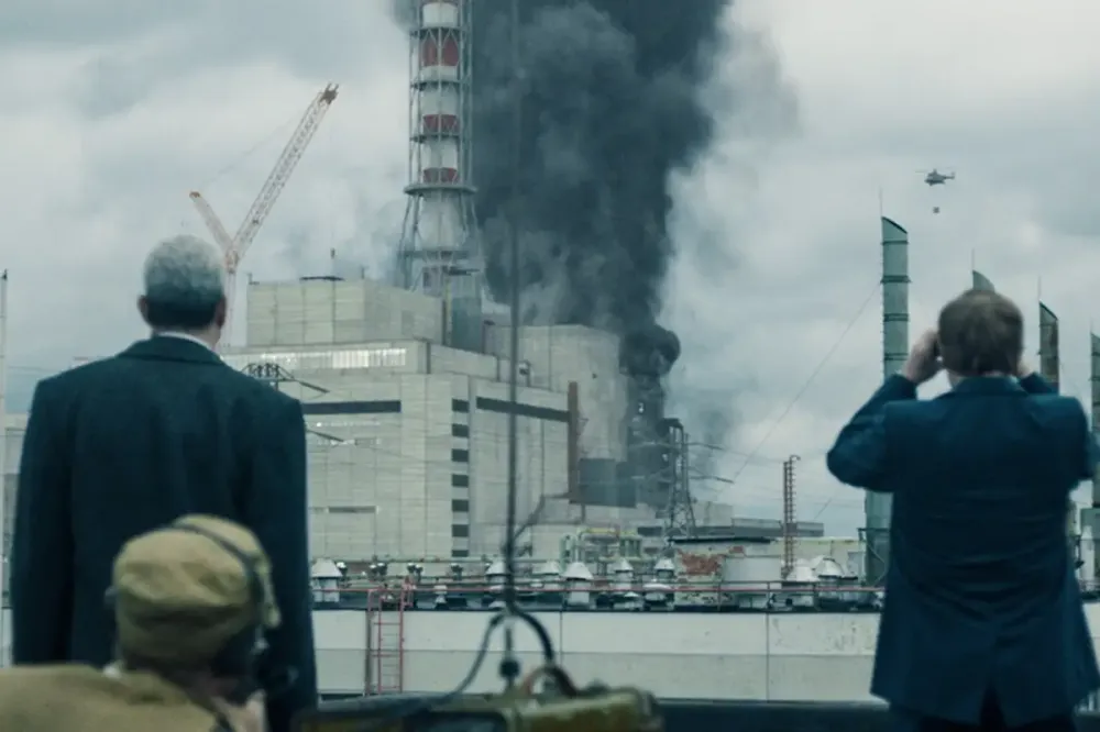 Three men stand before a burning nuclear power plant in 'Chernobyl.'