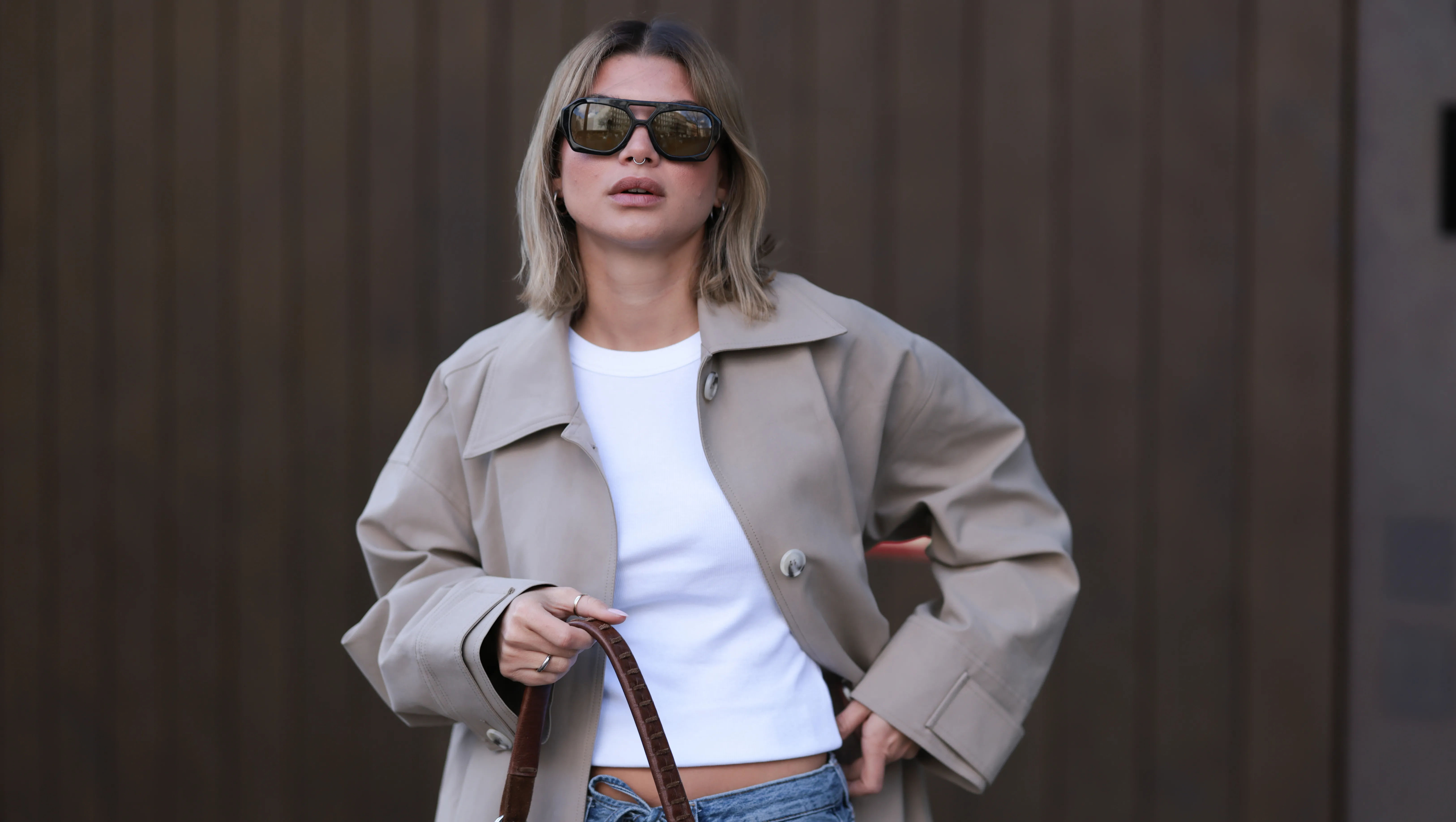 BERLIN, GERMANY - APRIL 01: Sophia Geiss seen wearing Vehla Eyewear black / brown dark sunglasses, Drykorn white cotton basic casual cropped top, Meotine beige oversized trench coat adds effortless elegance, COS blue denim oversized, loose-fitting, wide-leg jeans with a drawstring waist enhance the relaxed vibe and a brown suede leather vintage bag complements the western aesthetic, on April 01, 2025 in Berlin, Germany. (Photo by Jeremy Moeller/Getty Images)