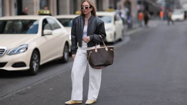 BERLIN, GERMANY - APRIL 09: Sonia Lyson seen wearing Linda Farrow bold white rectangular sunglasses that add a trendy touch, Zara white cotton fitted crop top, Zara high-waisted, wide-leg white relaxed jeans / denim pants, The Frankie Shop black, slightly glossy bomber jacket, Louis Vuitton brown Neverfull tote bag in the classic monogram print and Louis Vuitton beige Sneakerina sneakers / shoes with mustard yellow details, introducing a playful, sporty contrast to the otherwise minimalist outfit, on April 09, 2025 in Berlin, Germany. (Photo by Jeremy Moeller/Getty Images)