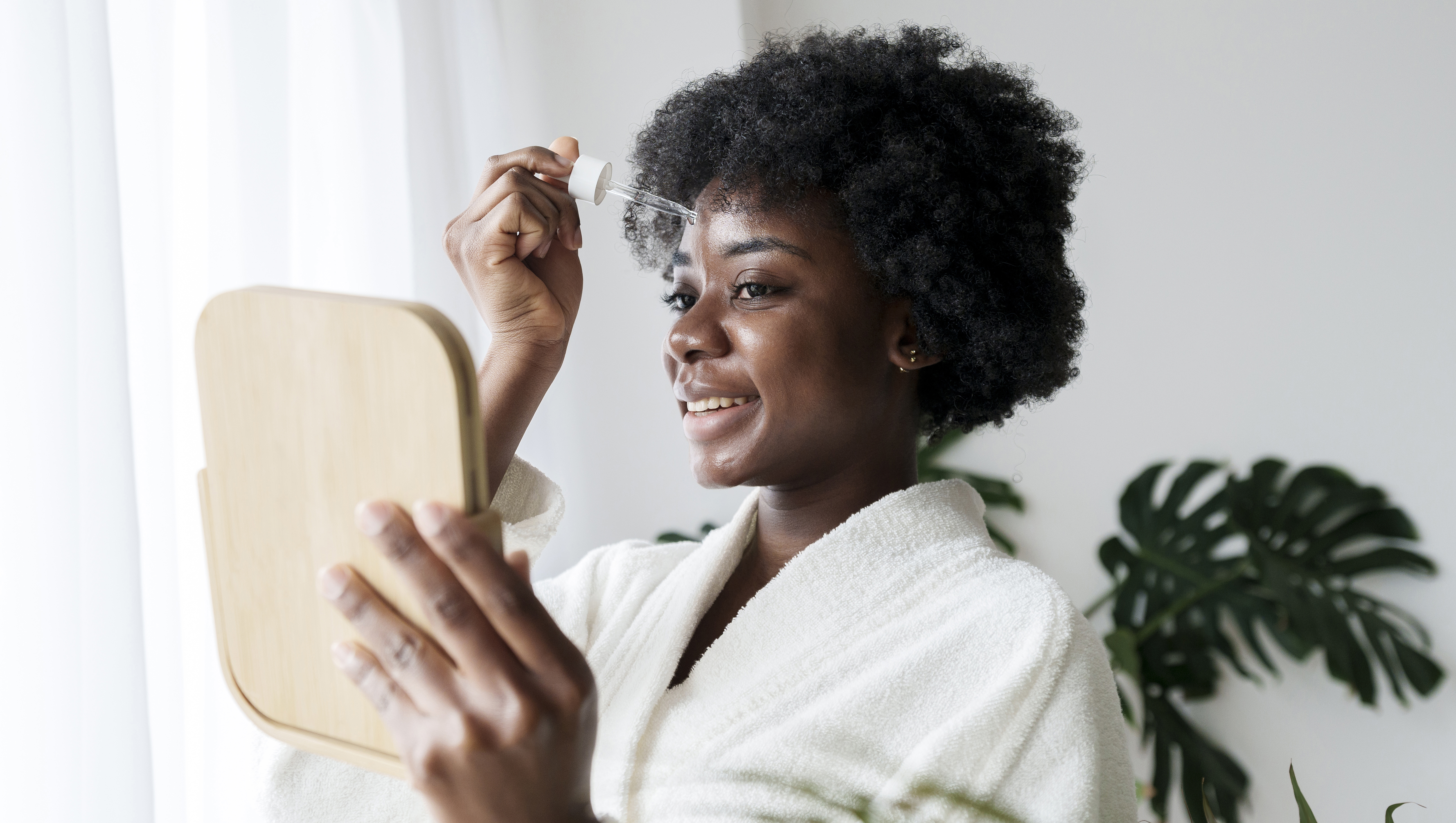 Happy young woman applying serum on face at home