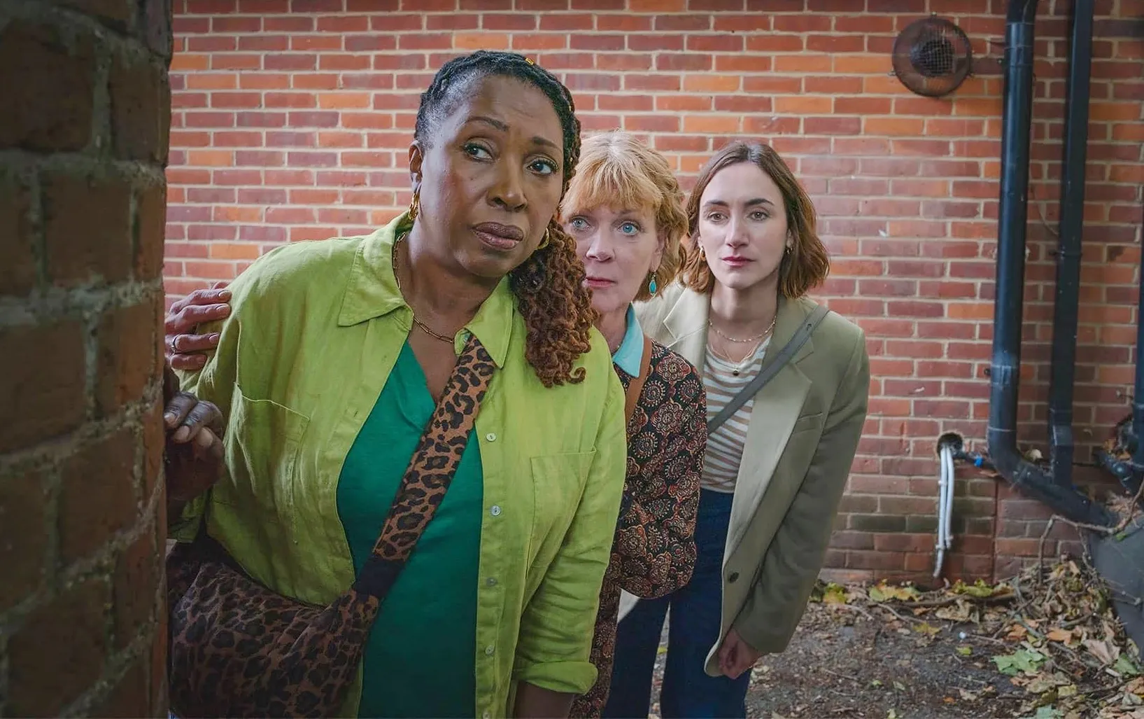 Three women lean near a brick wall in The Marlow Murder Club.