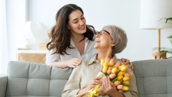 Beautiful young woman and her mother with flowers tulips in hands at home.