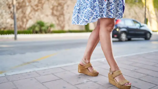 Legs of a woman in skirt standing on the street wearing sandals in closeup front view