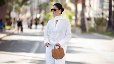 Gili Biegun wears white denim pants or jeans, white silk long sleeve shirt, brown leather bag and sunglasses during day three of the 78th Cannes Film Festival on May 15, 2025 in Cannes, France.