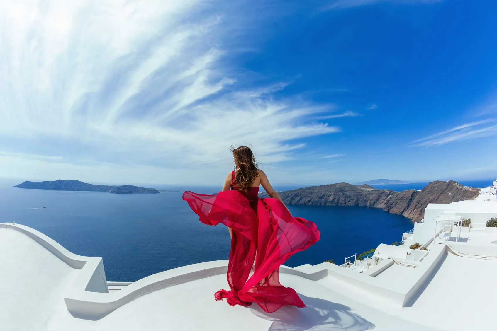 Woman in red dress aerial on the roof of island Santorini