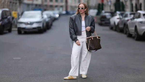 BERLIN, GERMANY - APRIL 09: Sonia Lyson seen wearing Linda Farrow bold white rectangular sunglasses that add a trendy touch, Zara white cotton fitted crop top, Zara high-waisted, wide-leg white relaxed jeans / denim pants, The Frankie Shop black, slightly glossy bomber jacket, Louis Vuitton brown Neverfull tote bag in the classic monogram print and Louis Vuitton beige Sneakerina sneakers / shoes with mustard yellow details, introducing a playful, sporty contrast to the otherwise minimalist outfit, on April 09, 2025 in Berlin, Germany. (Photo by Jeremy Moeller/Getty Images)