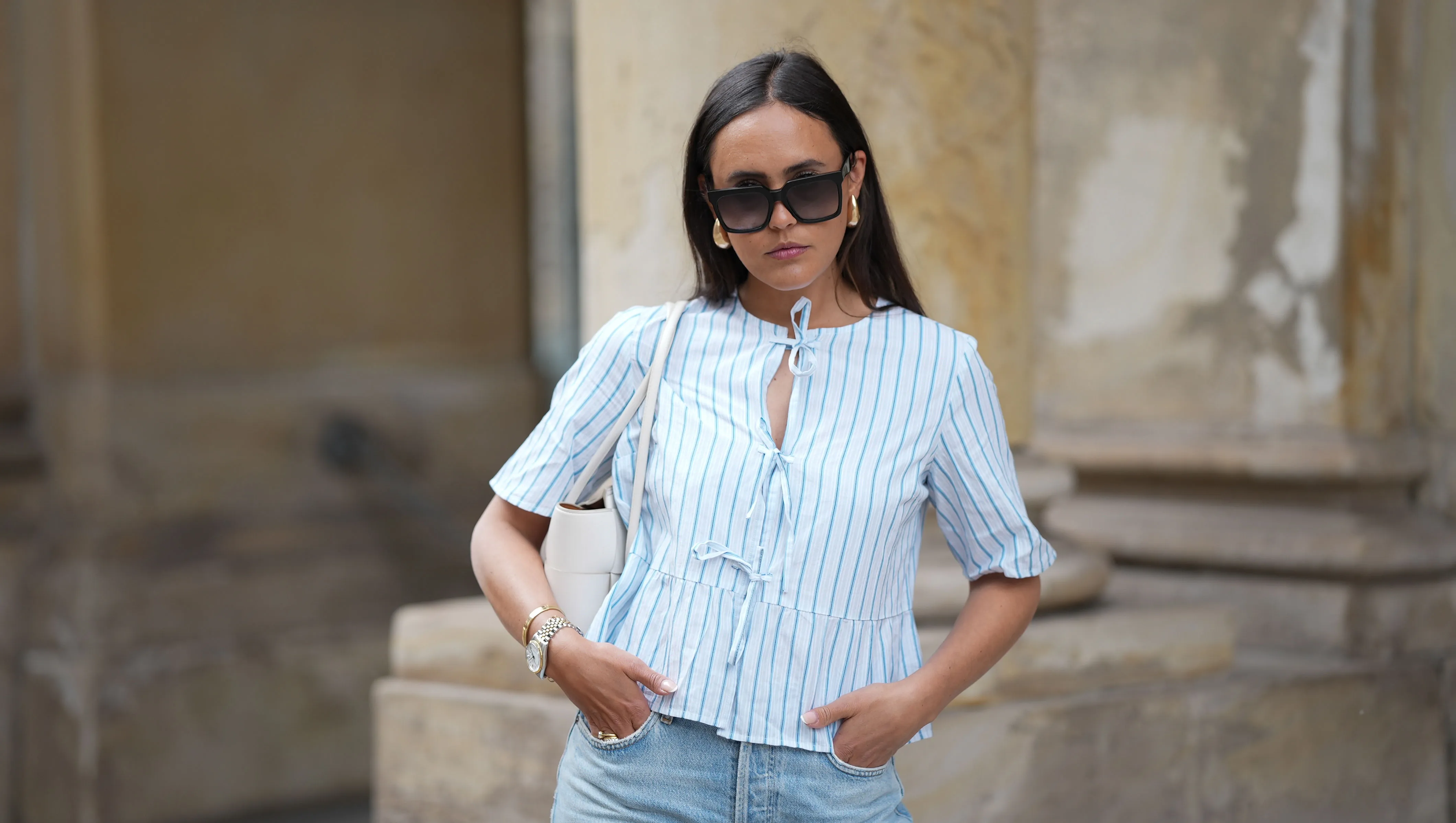 HAMBURG, GERMANY - MAY 7: Laura Noltemeyer is seen wearing a light indigo blue wide leg jeans from Agolde, a cotton puff sleeve blouse with ties in the front in white with blue stripes from Sézane, black oversized cat-eye acetate sunglasses from Celine, Arco handbag in white intrecciato leather from Bottega Veneta, big golden drop-shaped earrings, a small Lady-Datejust watch in gold-silver from Rolex, a golden LOVE bracelet from Cartier, stacked golden rings from Cartier on May 7, 2025 in Hamburg, Germany. (Photo by Moritz Scholz/Getty Images)
