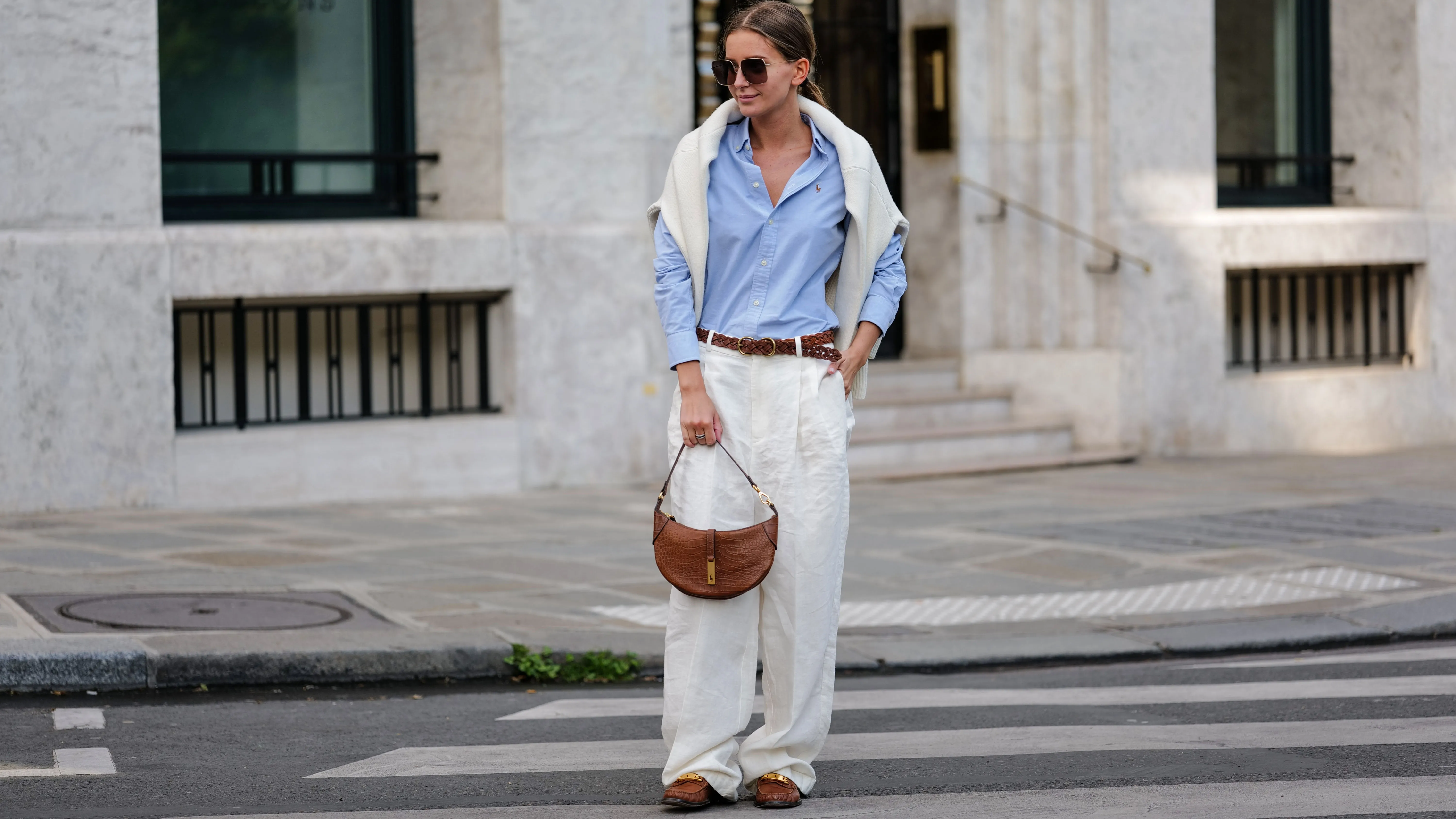 PARIS, FRANCE - APRIL 21: Diane Batoukina wears dark brown squared sunglasses from Dior, a pale blue cotton shirt from Ralph Lauren, a white matte large cashmere pullover from Weekend & Beyond, a brown braided leather belt from Ralph Lauren, white linen large pants from Ralph Lauren, a camel brown shiny leather crocodile print pattern handbag from Ralph Lauren, camel shiny leather with a gold metallic buckle loafers from Ralph Lauren, during a street style fashion photo session, on April 21, 2023 in Paris, France. (Photo by Edward Berthelot/Getty Images)