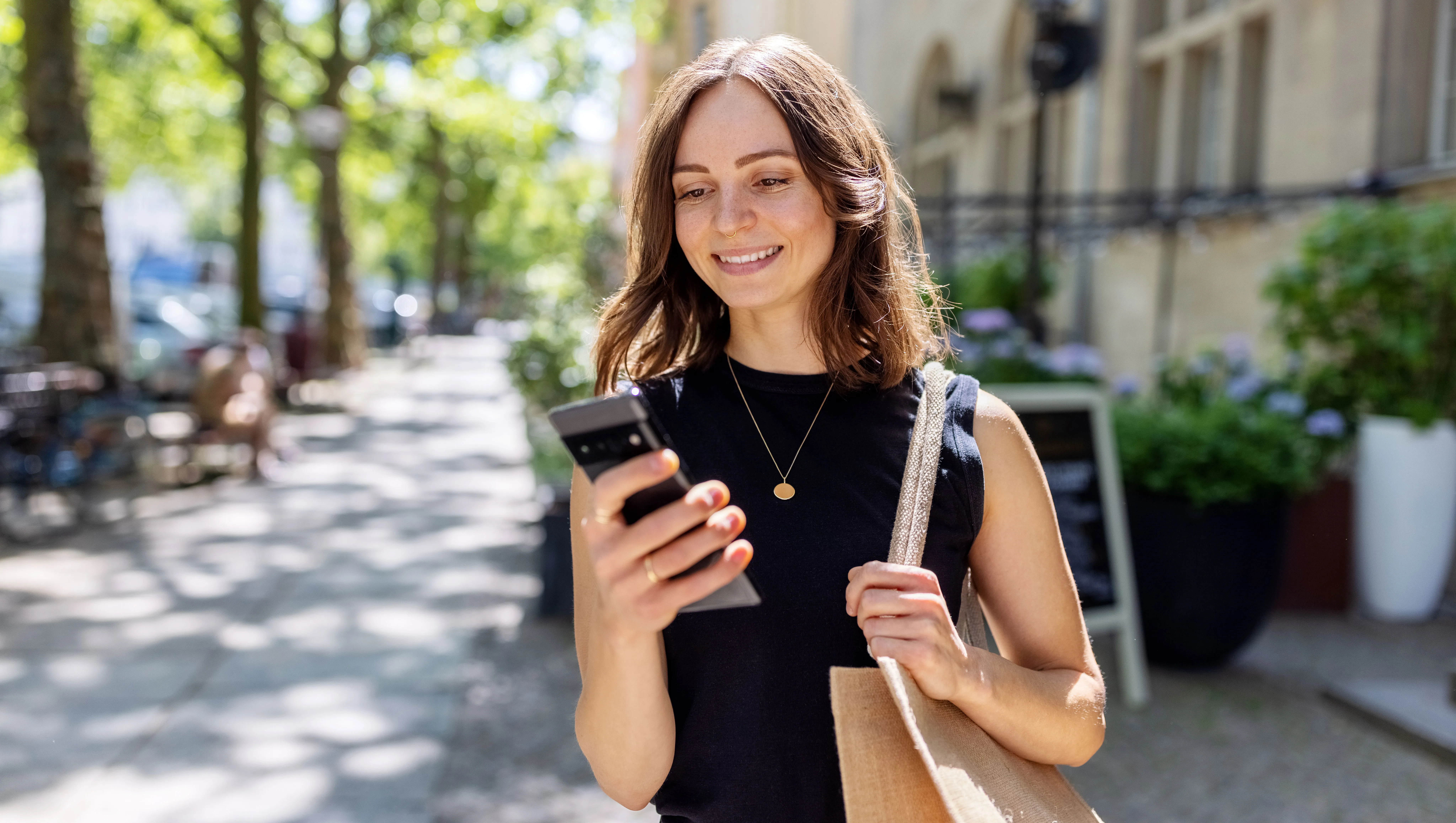 Smiling young woman with smartphone walking on the street - stock photo