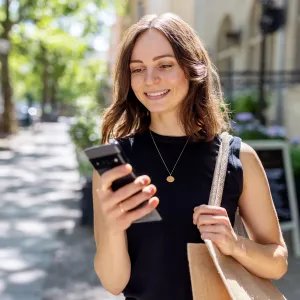 Smiling young woman with smartphone walking on the street - stock photo
