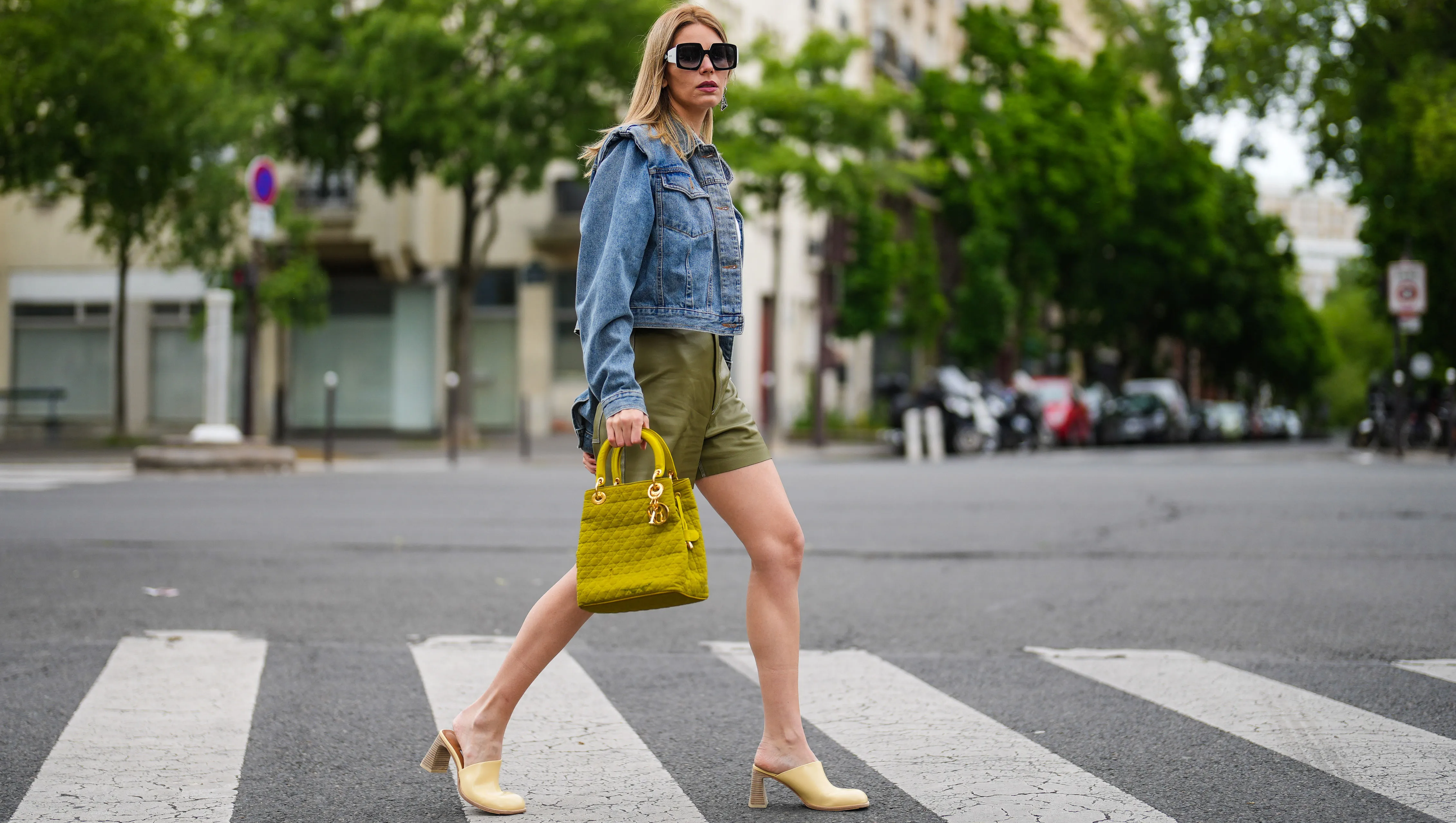 PARIS, FRANCE - MAY 16: Natalia Verza @mascarada.paris wears sunglasses from Pucci, a white t-shirt, a necklace, a blue denim jacket with shoulder pads from The Frankie Shop , green khaki mini leather shorts from Aeron, a khaki quilted bag from Dior, pale pastel yellow block heels shoes / mules from Miista, on May 16, 2021 in Paris, France. (Photo by Edward Berthelot/Getty Images)