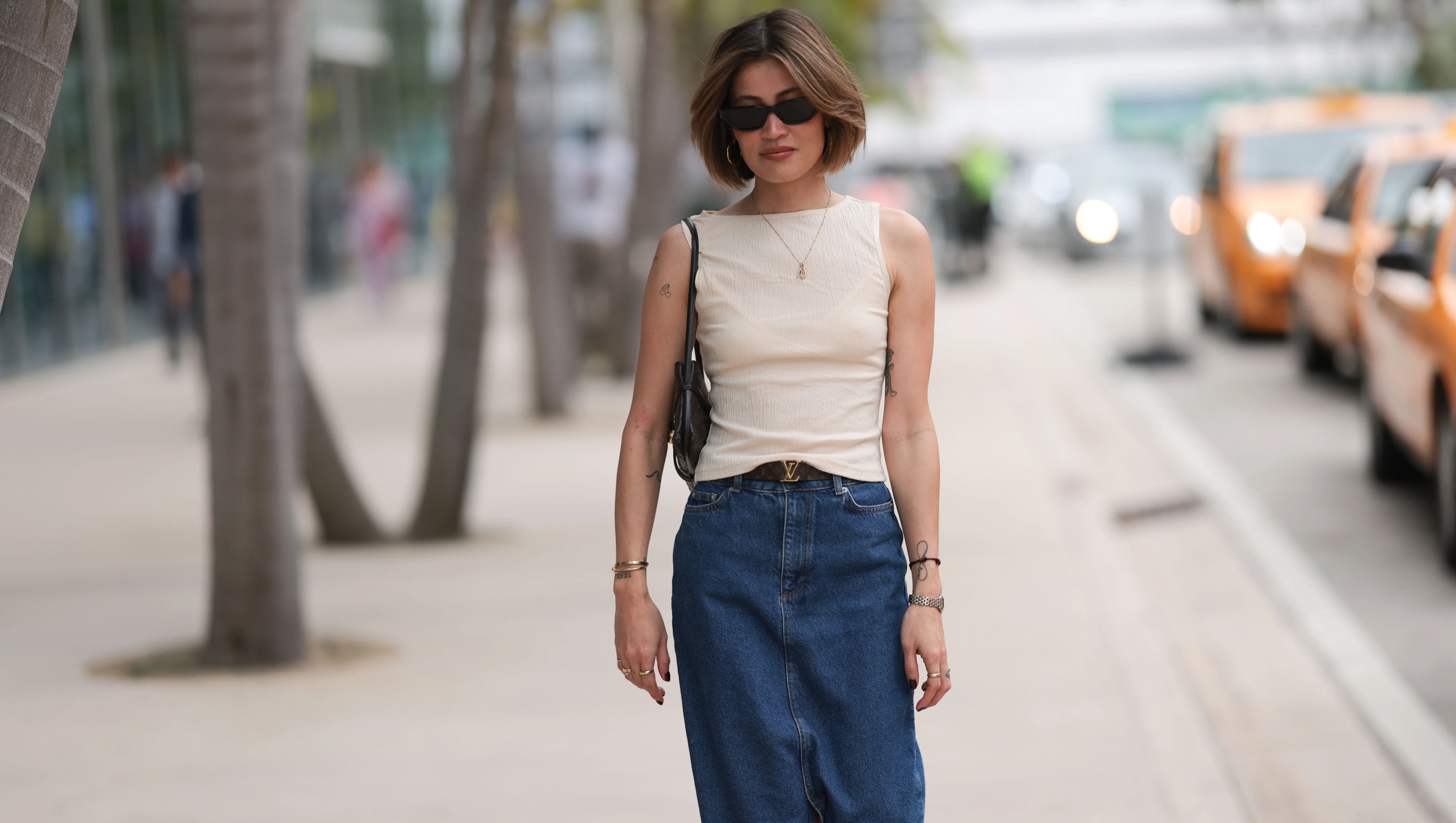 MIAMI, FLORIDA - DECEMBER 08: Michelle Fleur seen wearing Saint Laurent black sunglasses, cream white sleeveless top, gold letter necklace, Louis Vuitton brown canvas logo pattern belt, dark blue denim / jeans long skirt, Bottega Veneta black leather purse / shoulder bag, Cartier Panthère silver / gold bi-color watch, on December 08, 2023 in Miami, Florida. (Photo by Jeremy Moeller/Getty Images)