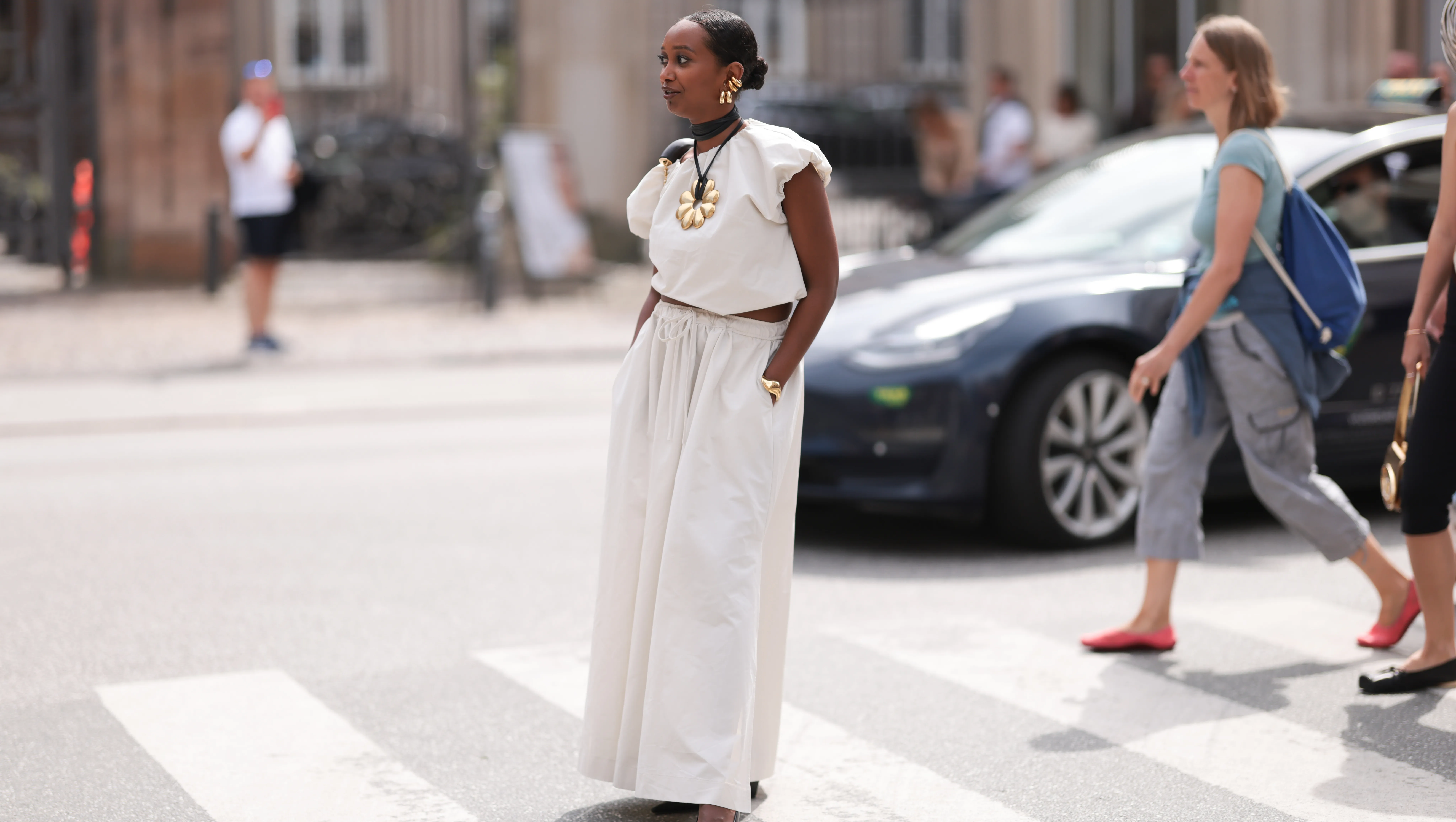 COPENHAGEN, DENMARK - AUGUST 07: Mona M. Ali is seen wearing huge golden hoop earrings from WOS, a black leather necklace with huge golden flower pendant from By Malene Birger, a white top with ruffled short sleeves from Gestuz, a white maxi skirt with front slit also from Gestuz, a golden bangle, a black leather bag from Loewe, and pointed black leather pumps before the Gestuz Show during the Copenhagen Fashion Week (CPHFW) SS25 on August 07, 2024 in Copenhagen, Denmark. (Photo by Jeremy Moeller/Getty Images)
