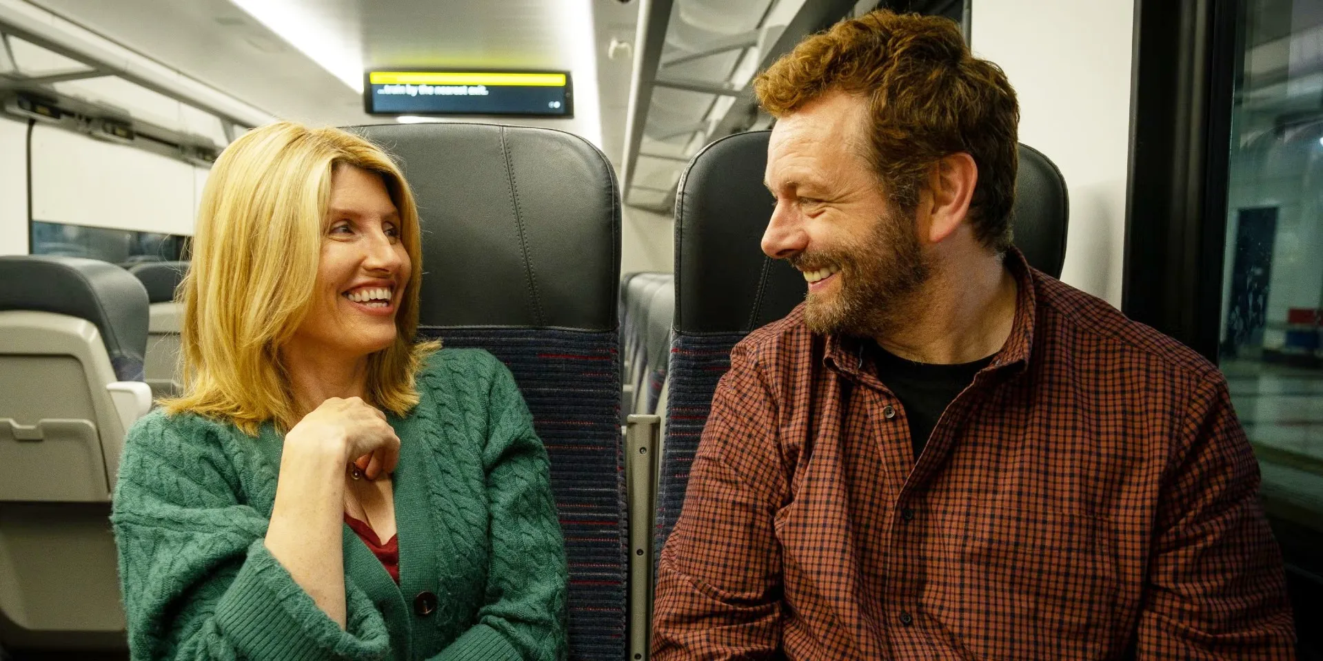 Two people smile on a train in 'Best Interests.'