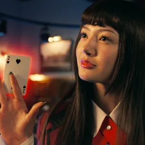 A woman holds a card in 'Bet.'