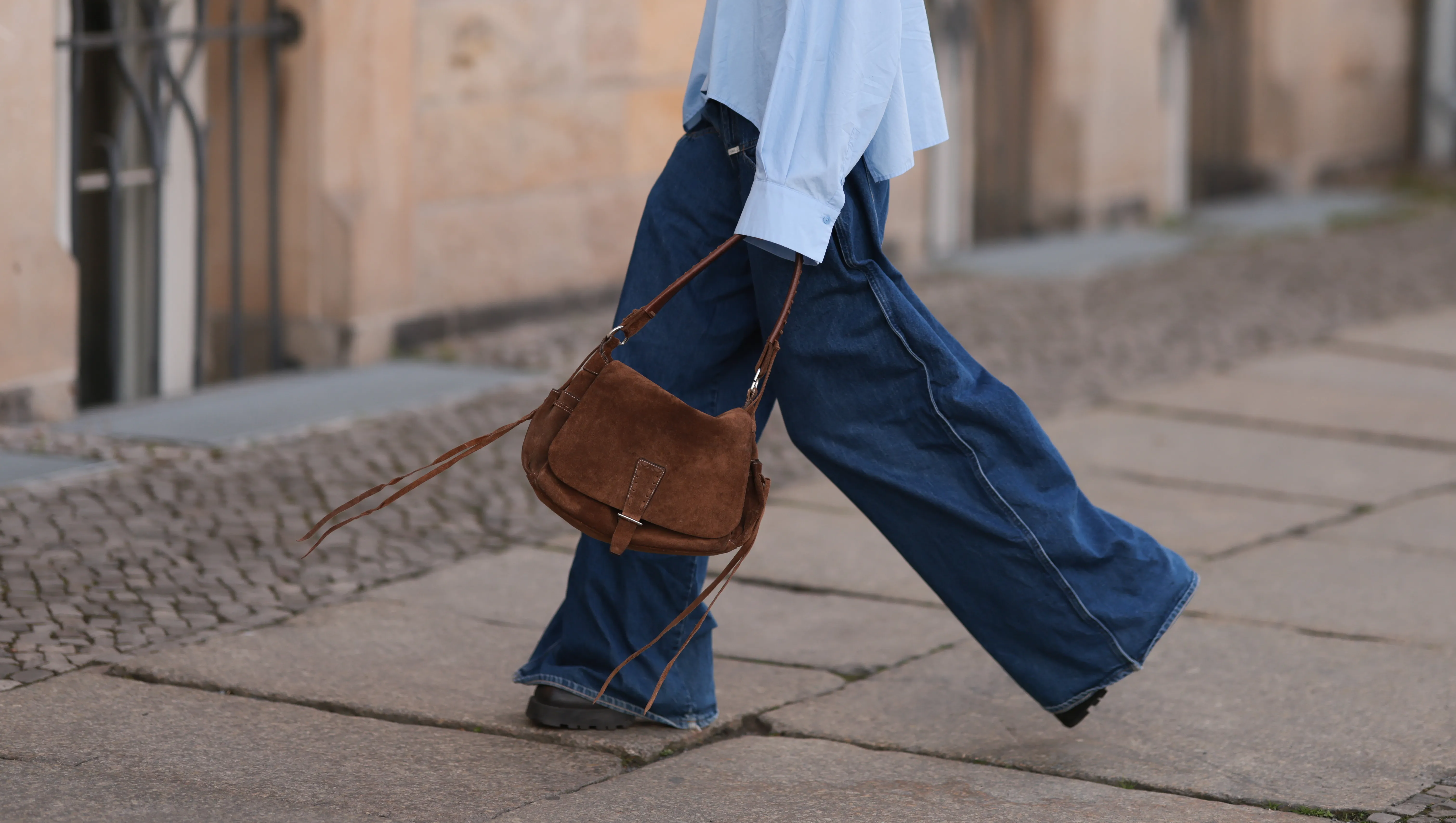 BERLIN, GERMANY - APRIL 22: Sophia Geiss is seen wearing two different-sized silver hoop earrings, oval brown glasses from Corlin, a silver nose ring, an oversized light blue shirt from Drykorn, wide-leg jeans with orange decorative seams from Closed, a brown vintage suede bag, and dark brown leather boots with chunky soles from Miista on April 22, 2025 in Berlin, Germany. (Photo by Jeremy Moeller/Getty Images)