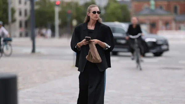 COPENHAGEN, DENMARK - AUGUST 08: Tine Andrea Lauvli is seen wearing an oval sunglasses with fine black metal frame, two fine gold necklaces, a black oversized blazer with 3/4 sleeves and a black pair of pants attached dangling from the top, a black top underneath, several gold bangles, a silver ring with rhinestones, a small brown fabric bag, blue wide-legged jeans, and pointed black leather heels before the Rotate Show during day four of the Copenhagen Fashion Week (CPHFW) SS25 on August 08, 2024 in Copenhagen, Denmark. (Photo by Jeremy Moeller/Getty Images)