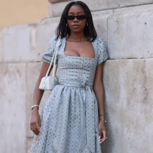 MUNICH, GERMANY - SEPTEMBER 21: Noutcha Lopes is seen wearing narrow rectangular sunglasses with a rounded black frame from Saint Laurent; chunky gold hoop earrings; a light blue dirndl with a flower pattern, a balconette neckline, a button placket, puffy short sleeves, and a bow from Limberry; a watch in silver and gold from Cartier; the yellow gold “Juste un Clou“ bracelet and ring from Cartier; a black bracelet with a blue eye pendant; and a rectangular white leather “Le Teckle“ bag with tubular handles from Alaïa during the opening day of the 2024 Munich Oktoberfest on September 21, 2024 in Munich, Germany. This year's Oktoberfest will run through October 6 and is expected to draw millions of visitors. (Photo by Jeremy Moeller/Getty Images)