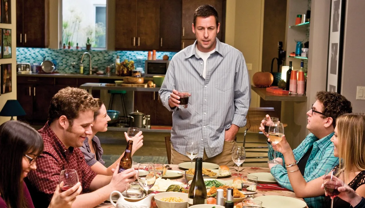 A man stands at a crowded table in 'Funny People.'