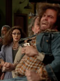 A group of actors look surprised as a man with a mustache holds back an angry man with curly hair in the movie 'Saturday Night.'