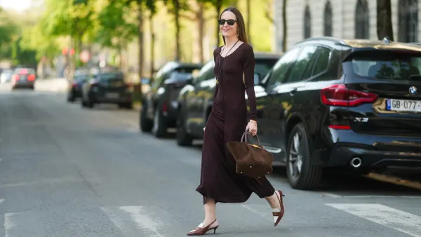 PARIS, FRANCE - APRIL 09: Alba Garavito Torre wears long, straight, brown hair with a middle part, natural complexion, subtle blush, and pink lipstick. Black rectangular sunglasses are worn. A brown tie-neck backless jersey long dress with long sleeves by Commense is styled with brown and white pointed slingback heels by Miu Miu. A mocha suede structured tote bag with double handles and gold clasp hardware by Demellier is carried by hand. A long leather necklace with a gold pendant and a delicate gold bracelet by Sempiterno Paris complete the look. Full body shot, during a street style fashion photo session, on April 09, 2025 in Paris, France. (Photo by Edward Berthelot/Getty Images)