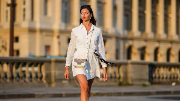 PARIS, FRANCE - AUGUST 21: Amanda Derhy wears black sunglasses, pearls pendant earrings, a gold chain pendant necklace, a white cut-out and lace flower pattern buttoned / shirt / belted short dress, a red with navy blue and white striped scarf, silver bracelets, a white moon stones bracelet, a beige matte and brown shiny leather with silver stars nailed / studded crossbody bag from Furla, white with pale pink heart Stan Smith sneakers from Adidas, on August 21, 2021 in Paris, France. (Photo by Edward Berthelot/Getty Images)