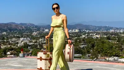 PARIS, FRANCE - MAY 13: Julia Comil wears a lime sorbet cropped linen cami top by Bondi Born, lime sorbet high waisted linen pants by Bondi Born, sandals by wandler, sunglasses by Lanvin, vintage hat box by Steamline luggage, vintage linen and leather cabin luggage by Steamline luggage, during an online remote street style fashion photo session via Apple iphone / Facetime and the CLOS app as the model is located in Beverly Hills - California and the photographer in Paris - France, on May 13, 2021 in Paris, France. (Photo by Edward Berthelot/Getty Images)