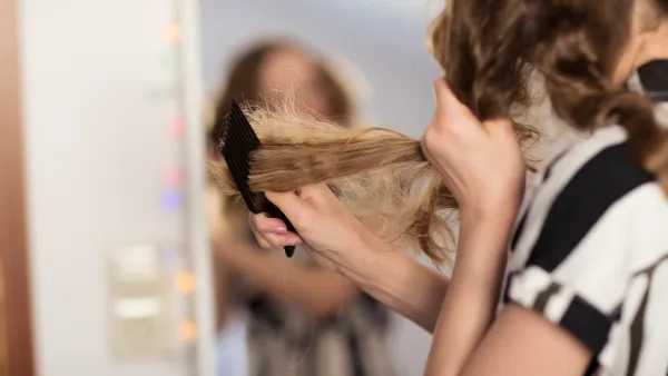 Teenage girl using comb to untangle dry, knotted hair